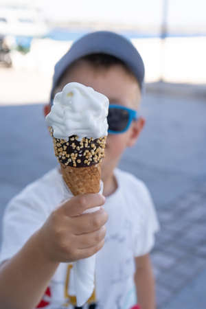 A boy in a cap and sunglasses holds an ice cream in his hand in the foreground