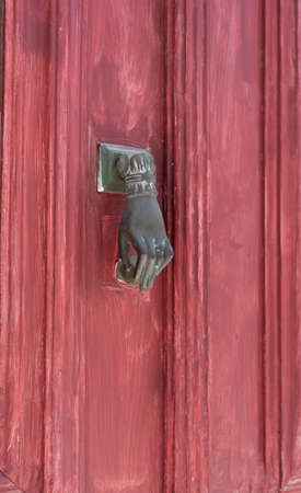 Doorknob in the shape of a woman's hand on a red door in Greece.
