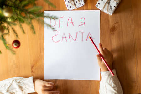 A little boy in a white sweater writes a letter with mistakes to Santa Claus. Top view, only hands in the frame.の写真素材