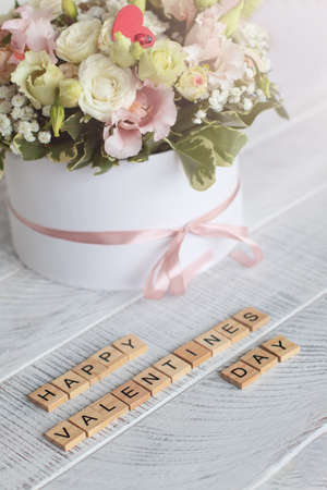 Flowers in a round box on a light wooden background and the inscription Happy Valentine's Day. vertical photoの写真素材