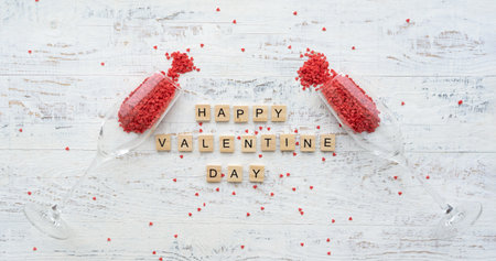 happy st. Valentine's day greetings card. Wooden letters on the white background with small scattered red hearts and overturned champagne glassesの写真素材