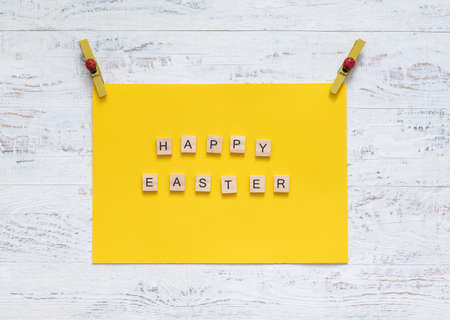 Wooden inscription Happy Easter on the yellow paper on clothespins. minimalism.