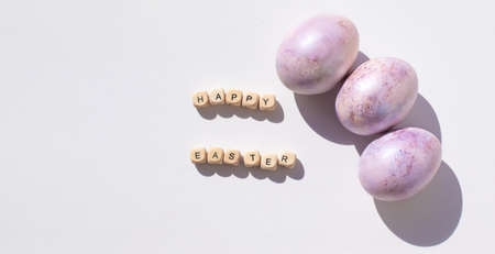 Easter concept banner. Purple eggs and wooden letters on a white background. Minimalism.の写真素材