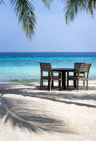 Wooden furniture of a restaurant in the shade of palm trees on the coast of the Maldives