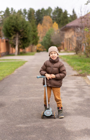 Little boy in jacket and hat and shorts is riding on the backdrop of an autumn landscapeの写真素材