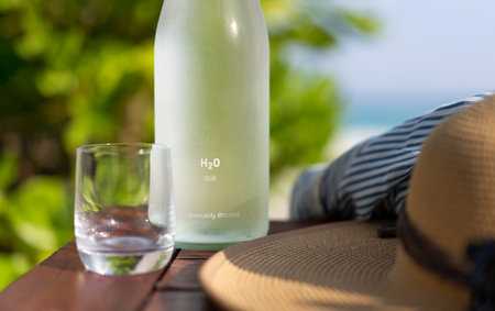 Glass bottle of water, straw hat and sun glasses on the background of the beach in the Maldives....