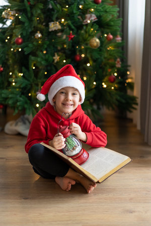 A little boy in a Santa Claus hat sits on the floor and reads a book with fairy tales.の写真素材