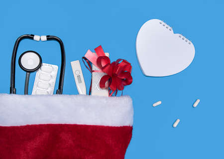 Medical Christmas card with pills, gift present box, mock up heart and Christmas hat on blue...