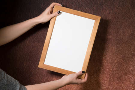 Woman's hands holding white wooden frame, dark background, mock-up, empty space