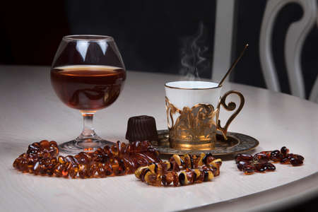 Cognac in tulip-shaped glass, amber jewelry and golden coffee cup on table, luxurious elegance style conceptの写真素材