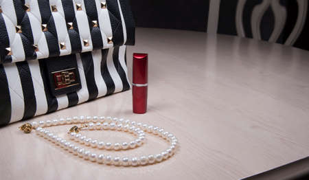Natural pearl necklace, striped woman purse and red lipstick on table. Fashionable style conceptの写真素材