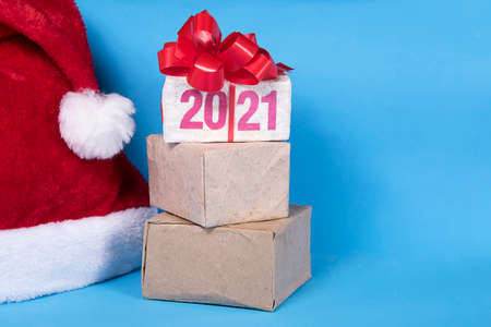 2021 text on gift box with red ribborn and santa claus hat. Blue background. Christmas and New Year purchase and retail concept. Copyspace.の写真素材