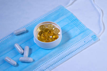 Round box with yellow food supplement oil filled capsules and group white cure capsule pills,...