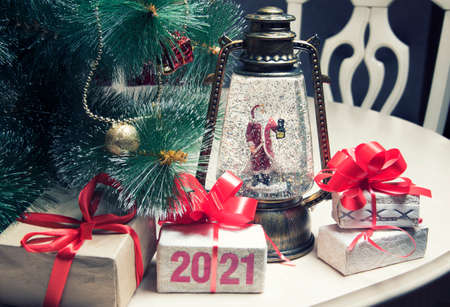 Christmas gift boxes with red ribbon, New Year tree with decorations, vintage magic lantern, toy santa on table in room. 2021 figures on box. Greeting card. Selective focusの写真素材