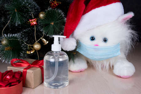 Christmas animals. Toy soft cat wearing Santa hat and medical face mask, sanitizer gel for covid-19. Coronavirus prevention concept at New Year holiday.の写真素材