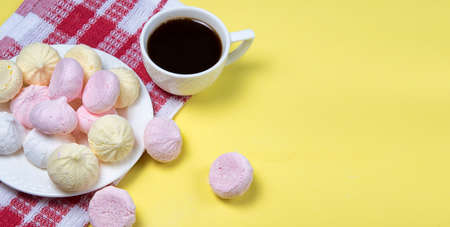 Small homemade meringue kisses. Banner with meringue cookies and coffee cup on red tablecloth and yellow background. Copyspace.の写真素材