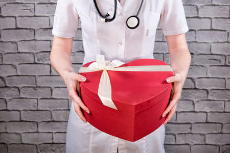 Doctor with red gift box heart shaped. Gratitude to physician concept. Congratulations for medics. Happy doctor's day present box.の写真素材