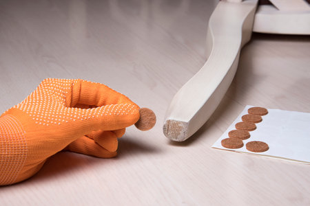 Hand stick floor care pad at chair wooden legs. Anti-skid felt pad cover sticking on wooden furniture leg. Installation chair and sofa protector.の写真素材