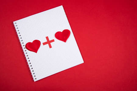Heart plus heart. Two red hearts on white notebook squared paper, red background, lovers together...