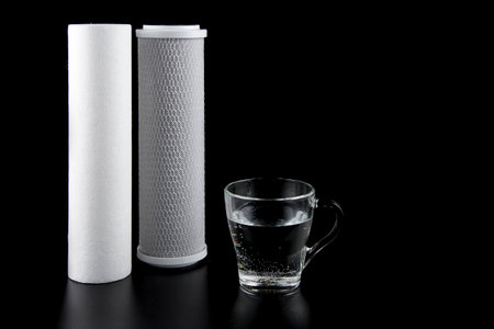 Water filters. Carbon cartridges membrane for water filtration RO (reverse osmosis) and glass isolated on black background. Household filtration system.の写真素材