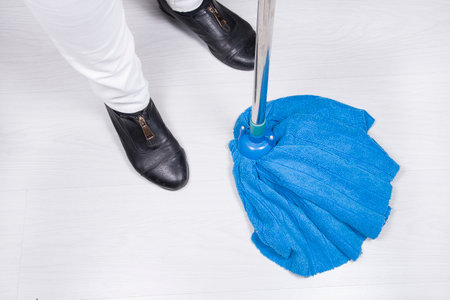 Close up of cropped view of female legs with blue mop. Washing floor. Domestic home cleaning. Cleaning service concept at home, apartments, hotels. Maid or housewife washing roomの写真素材