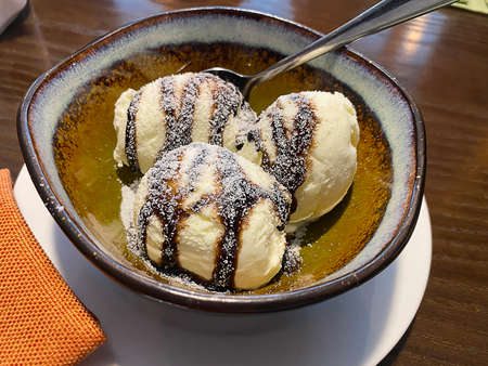 Three melting chocolate ice cream balls in brown ceramic bowl on table in cafe