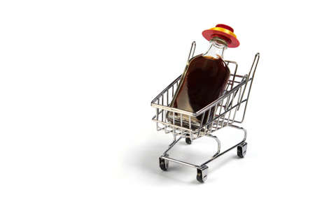 Small wine bottle with red hat in mini shopping cart isolated on white background. Alcohol delivering conceptの写真素材