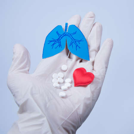Paper lungs, red heart and white pills on doctor's gloved hand, blue background. World Tuberculosis Day.の写真素材