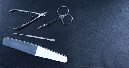 Set manicure tools on black stone background. Scissor, pusher, polisher and clipperの写真素材