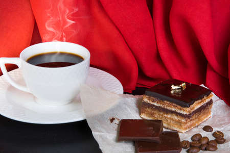 Chocolate cake named âParis Operaâ and white coffee cup. Classic french "Opera" cake. Home cooking. Red fabric background.の写真素材