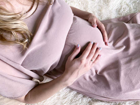 Pregnant woman touching belly lying on white bed