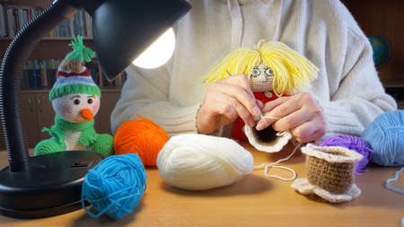 Female hands holding crochet hook. Woman knitting homemade toys in dark room under lamp. DIY hobbies.の写真素材