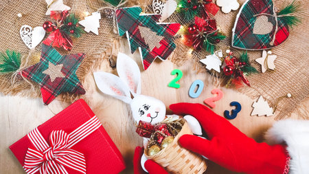 Christmas background with trees, stars and gift box. Hands putting rabbit. 2023 figures. New Year decorations on wooden background. Flat lay, top view.の写真素材