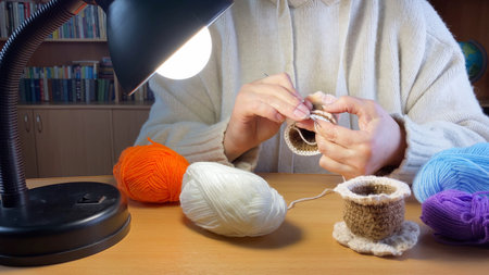 Female hands holding crochet hook. Woman knitting homemade things in dark room under lamp. DIY hobbies.の写真素材