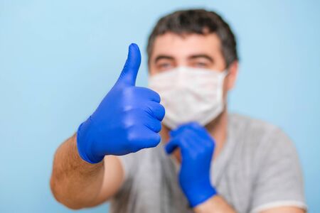 A man in a medical mask and blue medical gloves. Hand gesture class. Blue background.の写真素材