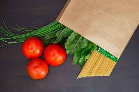 Food in a paper bag on a wooden table. Tomatoes, green onions, macaroni.の写真素材