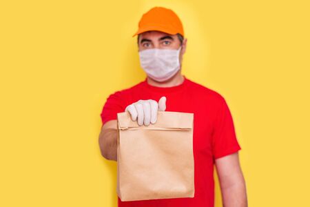 A courier employee in uniform holds a cardboard box with food isolated. Service quarantine pandemic coronavirus.の写真素材