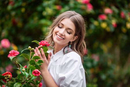 Beautiful woman with spring blooming pink flowers. A young smiling girl enjoys the pink flowers of a rose. Summertime.の写真素材