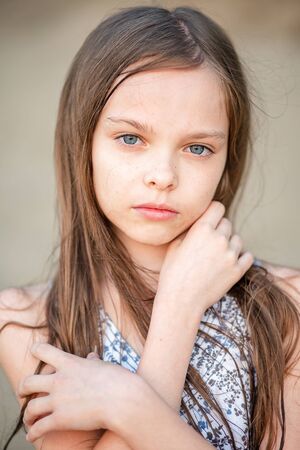 Portrait of a sad little beautiful girl with long hair. Girl 7-9 years old hands at the face.の写真素材