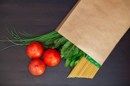 Food in a paper bag on a wooden table. Tomatoes, green onions, macaroni.の写真素材