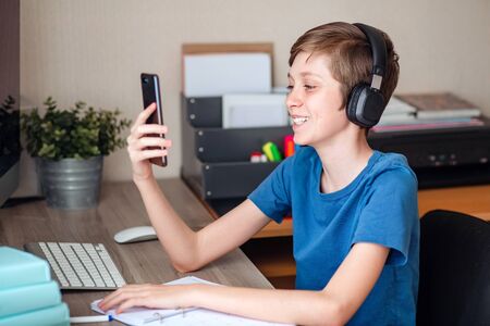 A teenage boy makes a video call using his mobile phone to his friends, classmates, and relatives....