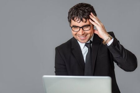 A male businessman in a black suit and glasses with a laptop. Happy with the good news. Talking...