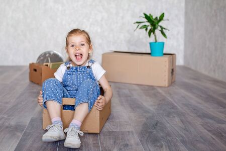 A little blonde girl plays at home in quarantine with cardboard boxes. The child moves to a new...