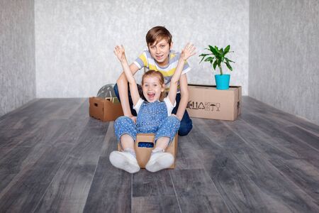 Brother rides sister in a cardboard box. Children play with boxes at home in quarantine. A boy and a...