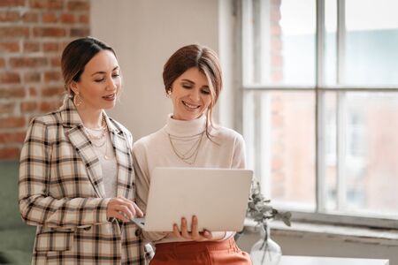 One-on-one meeting.Two young business women sit at a Desk in the office. The girl shows her colleague information on the laptop screen. Women discuss their work online and blog.の写真素材