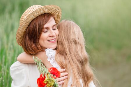Mother and daughter walking in the field. A blonde girl with long hair gives her mother a bouquet of poppies for mothers day.の写真素材