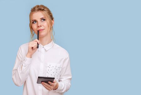 Portrait of an attractive young blonde woman with blue eyes working on a tablet. A young female entrepreneur freelance designer pondered the project, blue isolated background.の写真素材