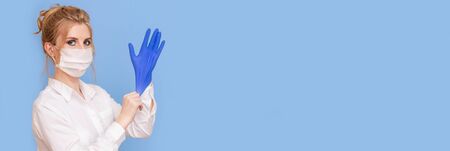 Young beautiful woman doctor in medical mask and gloves. The doctor is preparing to work in uniform. Respect for social distance and protection measures. Bannerの写真素材