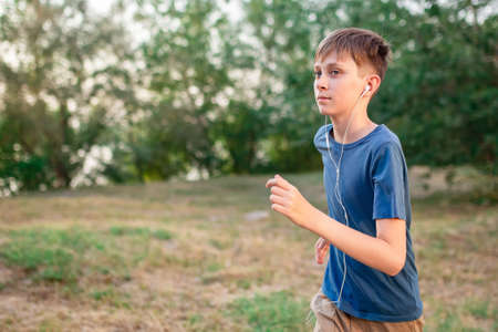 A teenage boy runs in nature with headphones listening to music. Active lifestyle of children and...