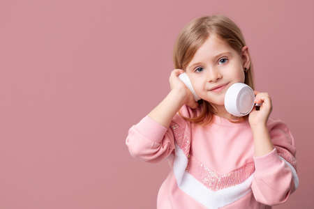 A little blonde girl listens to music with headphones, online distance learning on a pink isolated...
